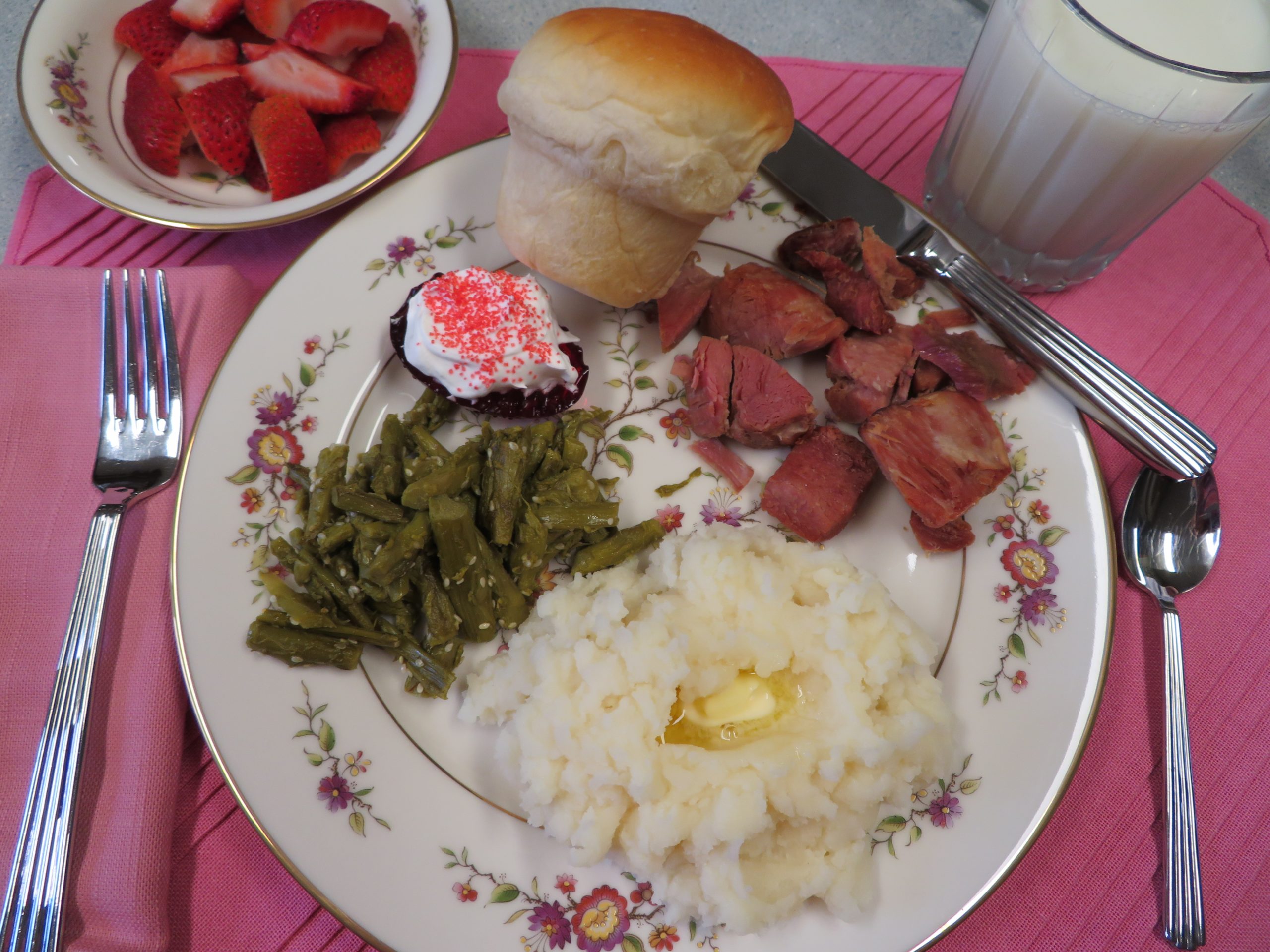 Easter dinner of baked ham, mashed potatoes, roasted asparagus, a Jello egg with whippe topping, homemade roll, and strawberries