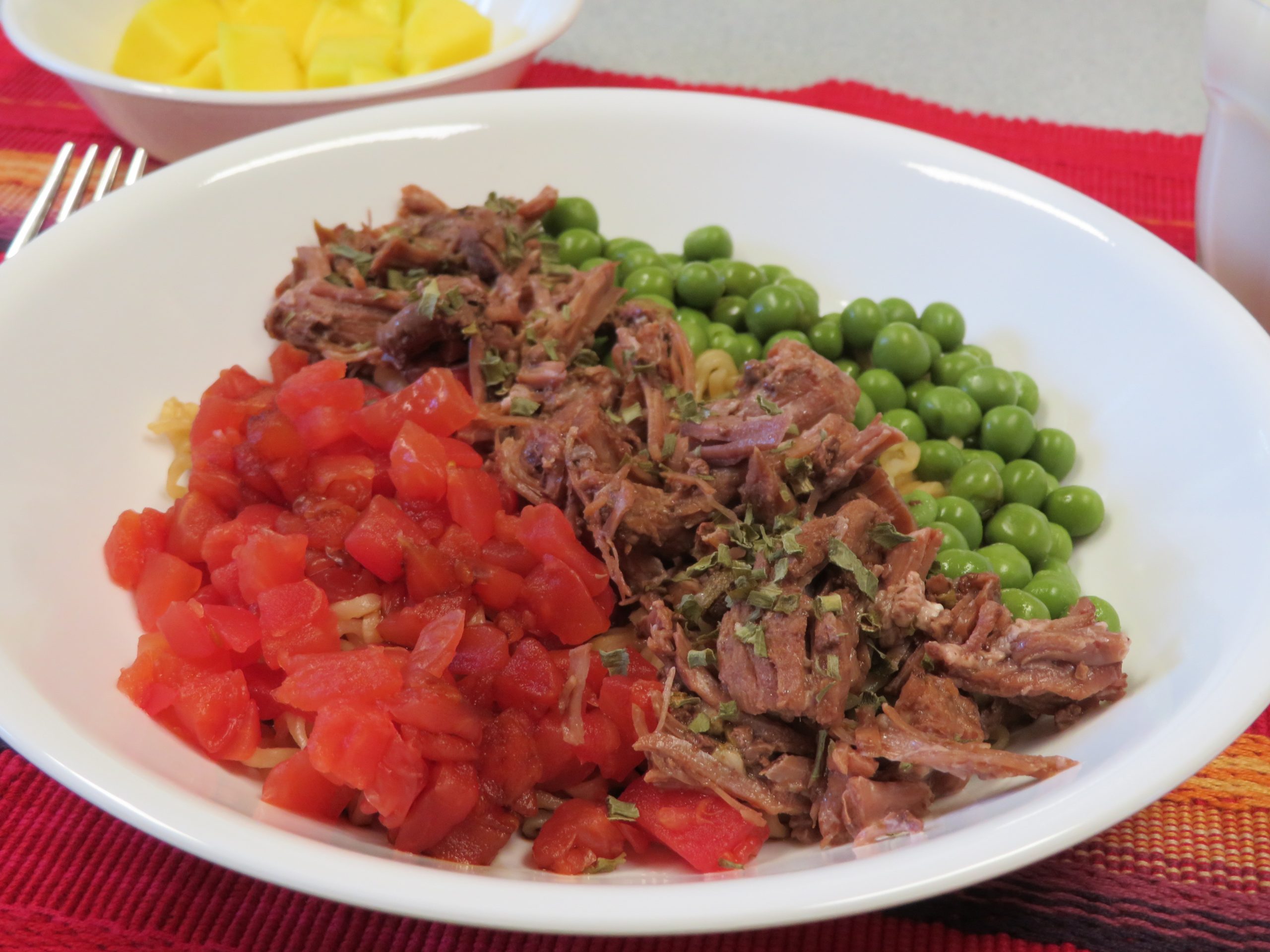 A bowl of ramen noodles with diced tomatoes, beef, peas, and dried chives