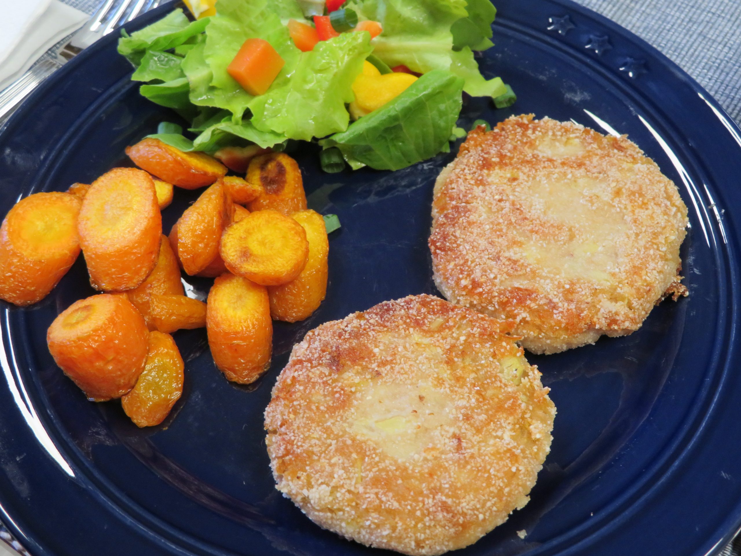 Artichoke cakes on a blue plate with roasted carrots and tossed salad