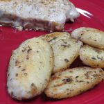 Herb roasted potatoes on a red plate with green beans and a pork chop