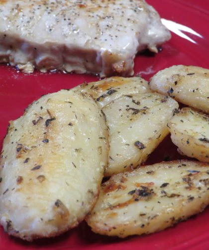 Herb roasted potatoes on a red plate with green beans and a pork chop