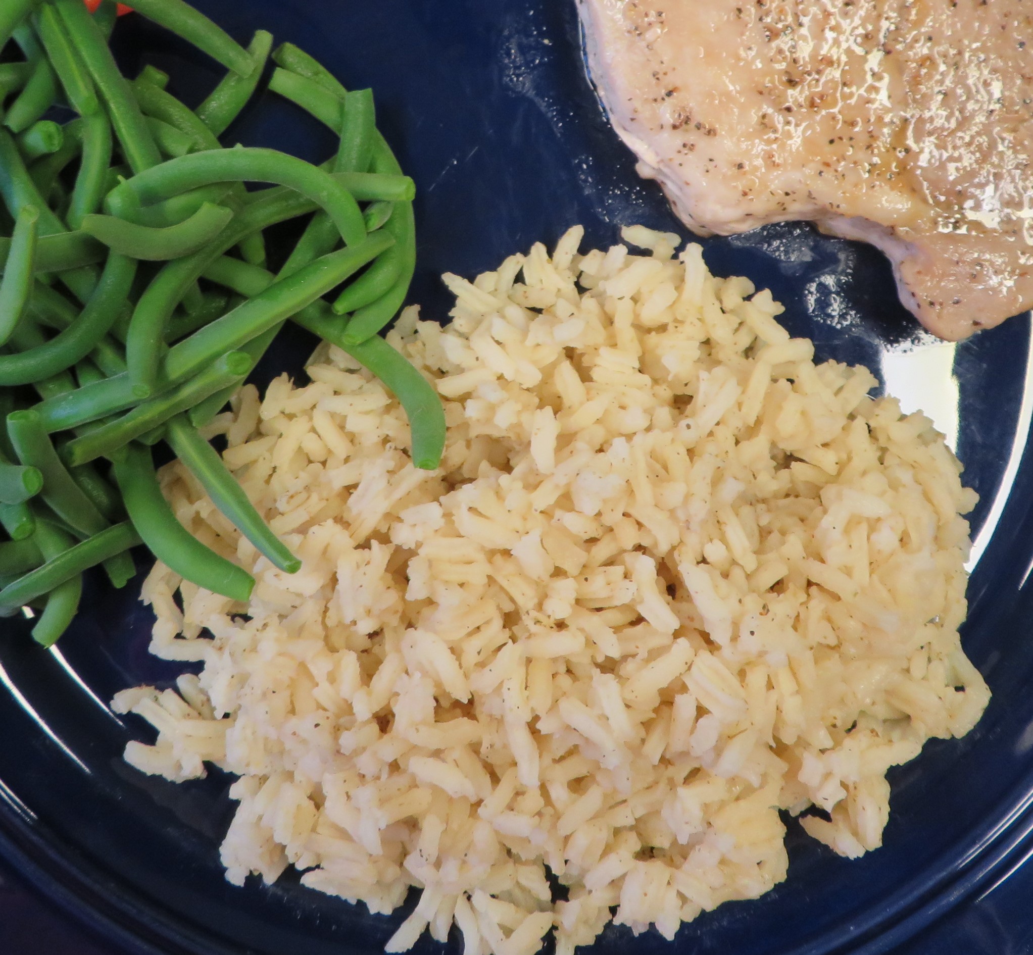 Tex Mex Seasoned Rice on a plate with green beans and a pork chop