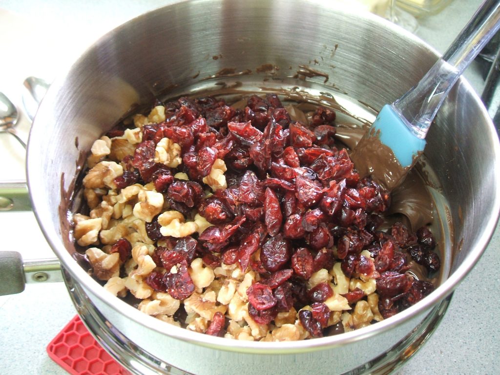 Double boiler with melted chocolate, walnut pieces, and dried cranberries.