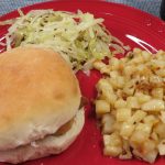 Roasted potatoes on a red plate with a sandwich and slaw