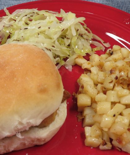 Roasted potatoes on a red plate with a sandwich and slaw