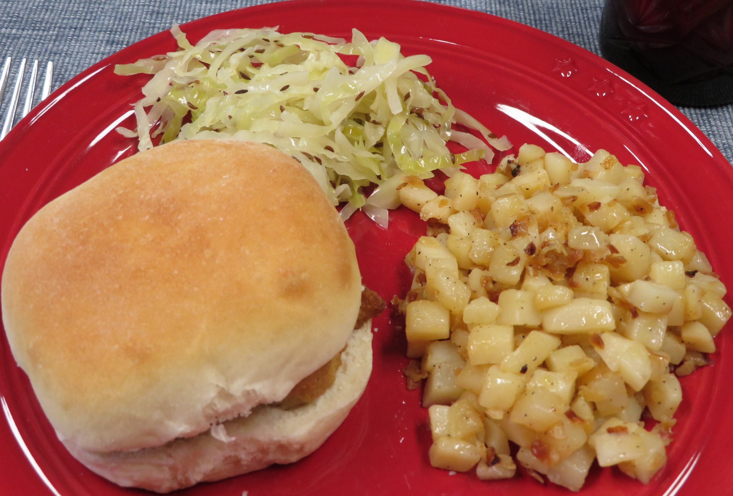 Roasted potatoes on a red plate with a sandwich and slaw