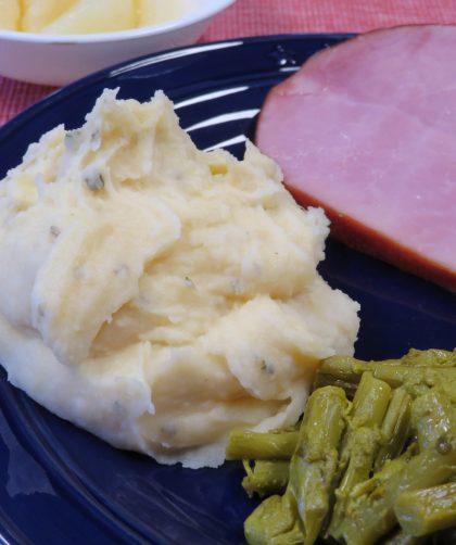 Cheese and chive mashed potatoes on a dinner plate with sliced ham and asparagus