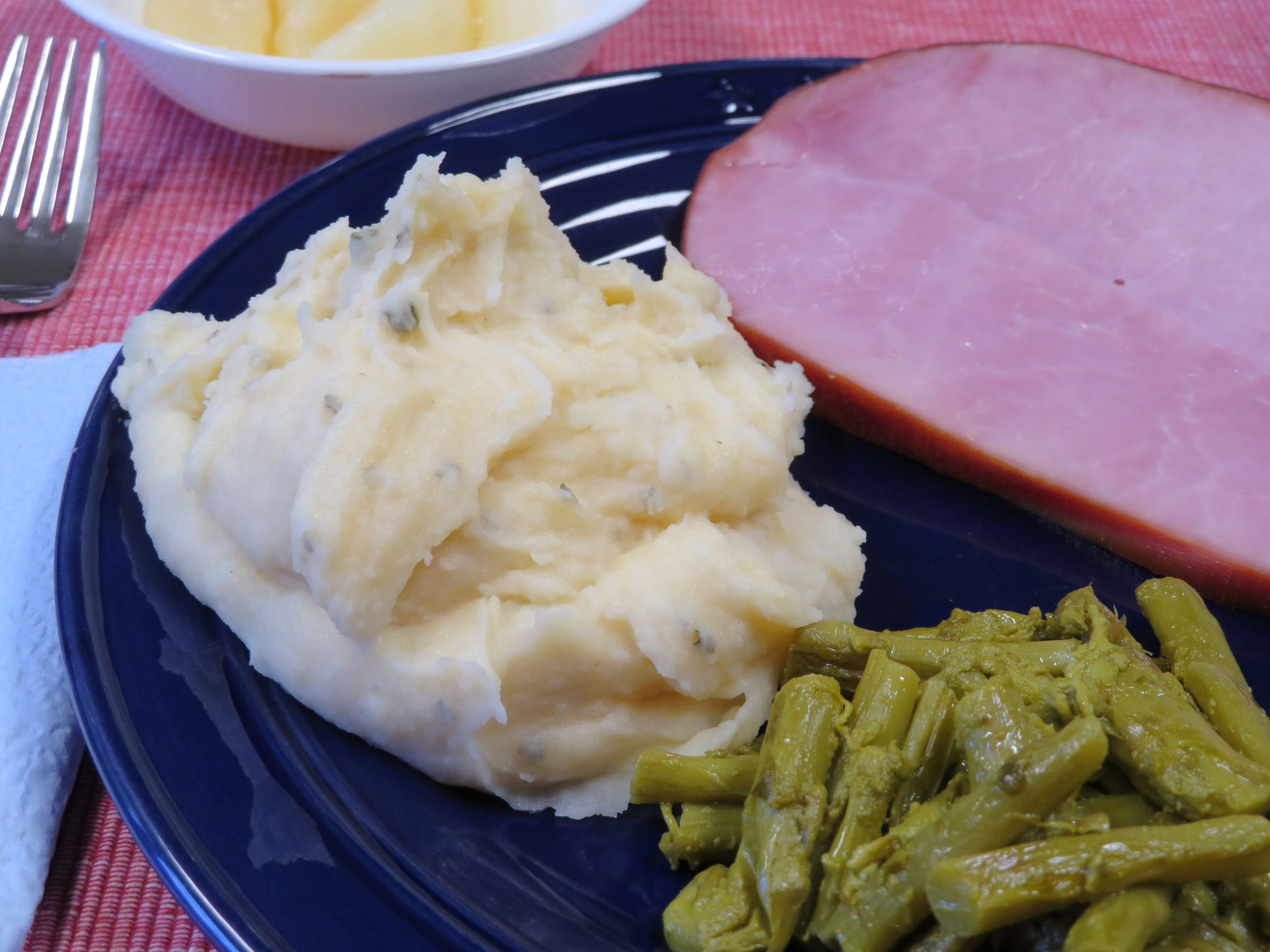 Cheese and chive mashed potatoes on a dinner plate with sliced ham and asparagus