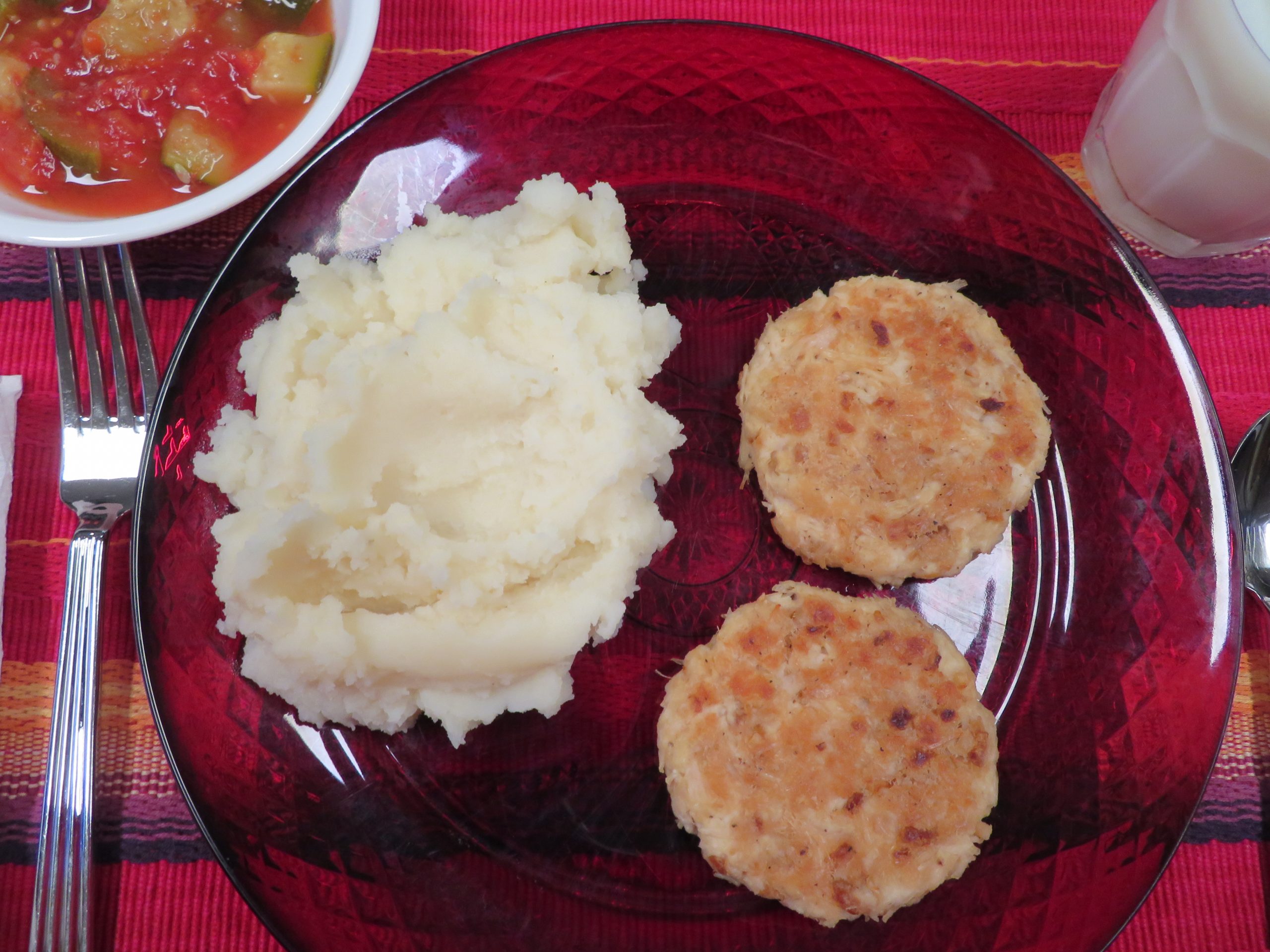 Dinner of chicken patties, mashed potatoes, tomatoes and zuchinni, and milk