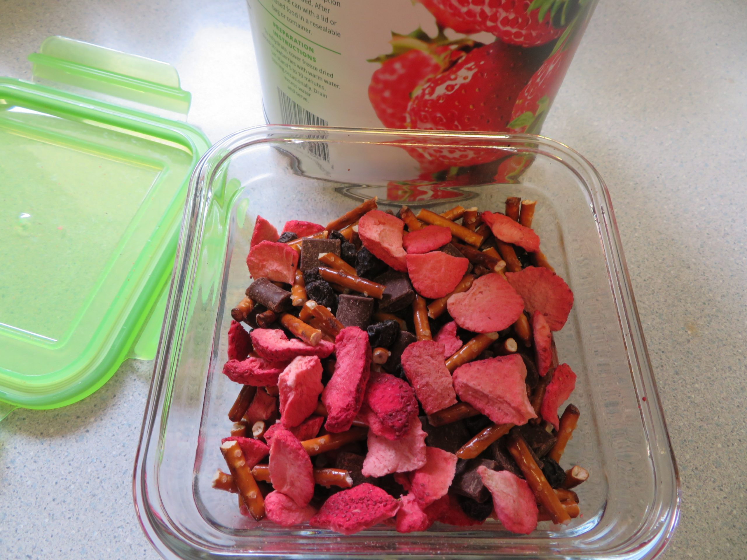 Strawberry snack mix beside the container lid and strawberry can