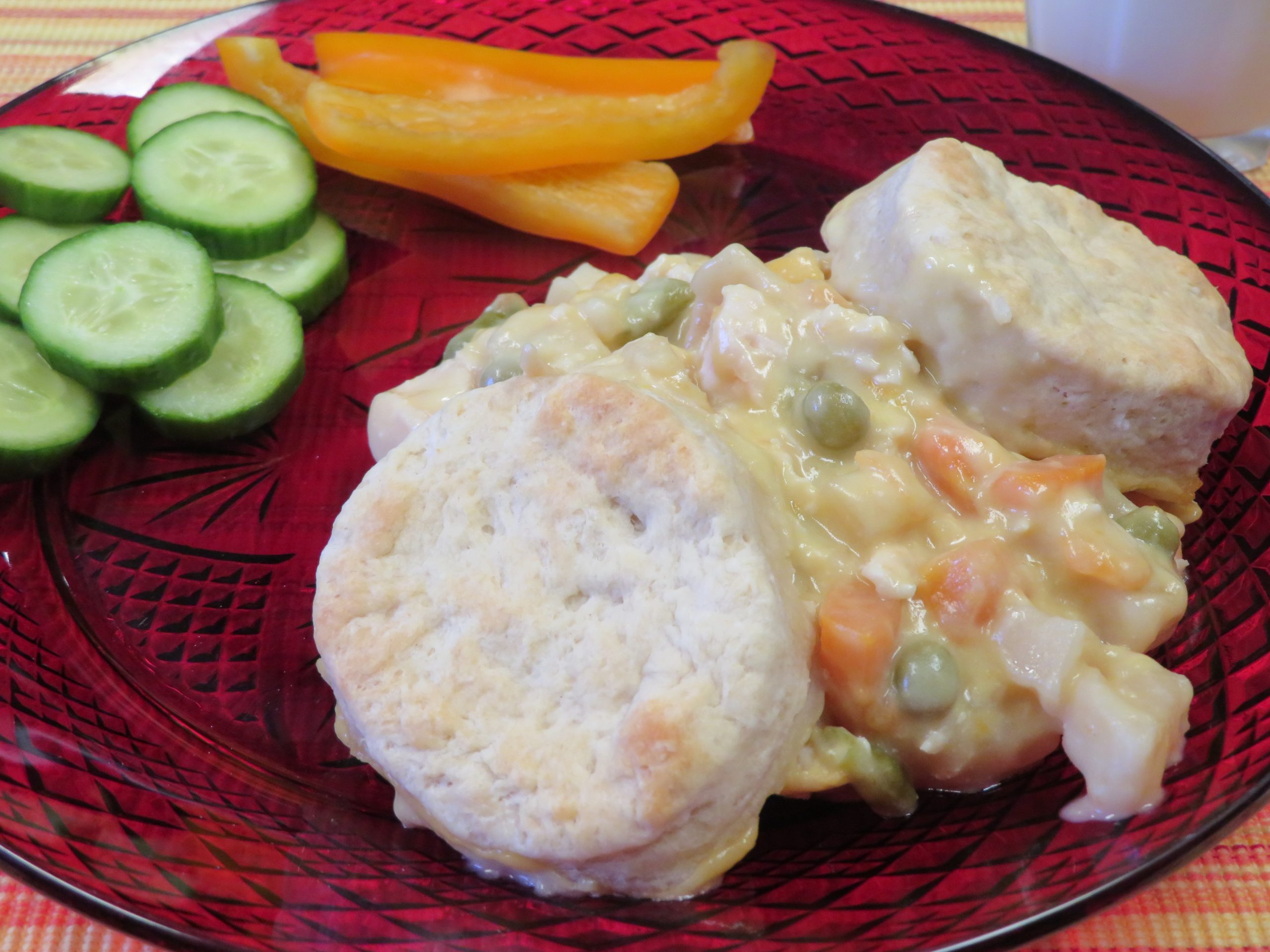 Chicken Pot Pie on a red plate with sliced cucumbers and orange bell pepper sticks