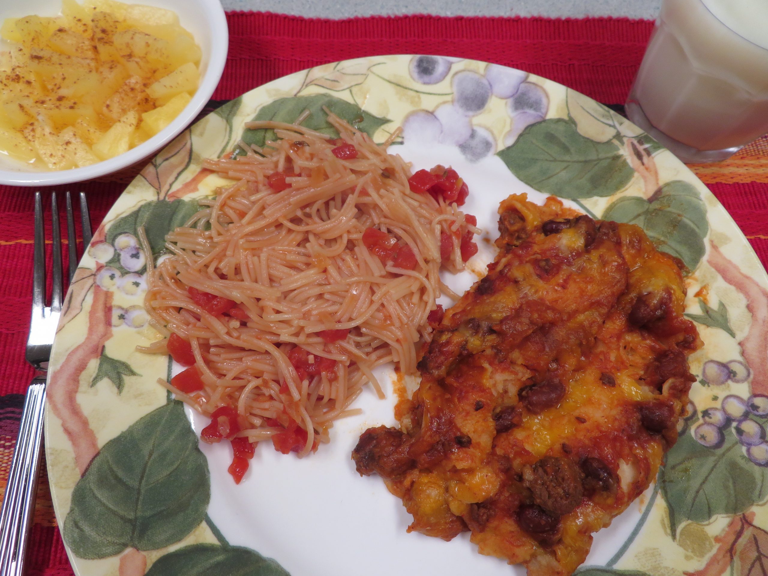 Dinner plate with Pantry Fideo and enchiladas, glass of milk, bowl of pineapple