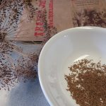 Paper sack, dried dill seed head, and harvested seeds in a bowl