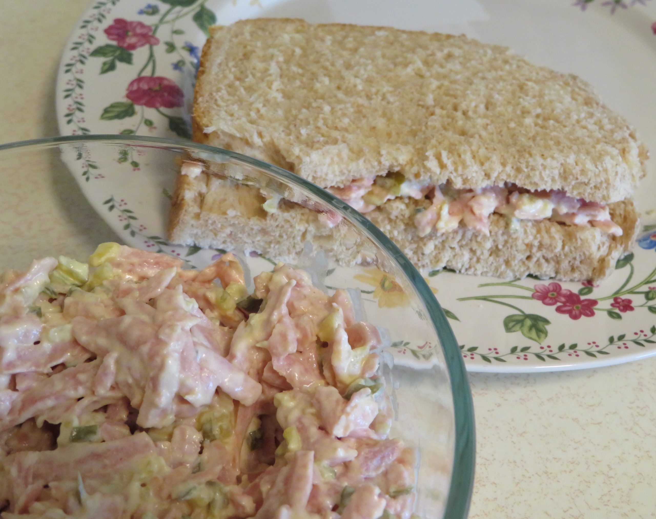 Dill Spam Salad in a glass bowl and a sandwich on a floral edged plate