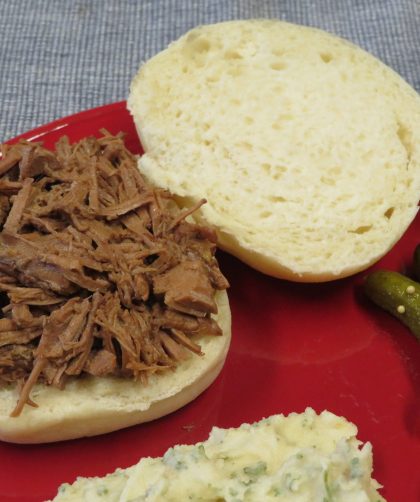 Smoked Brisket sandwich on a red plate with Mashed Potato Salad, pickles, and cut up vegetables